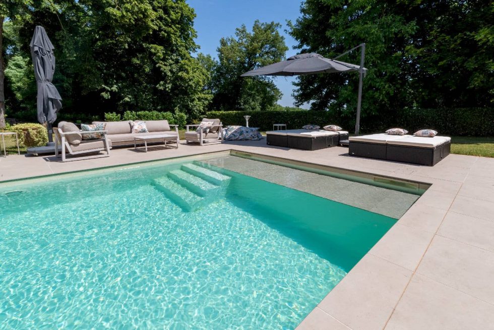 Mobilier de détente, bains de soleil et parasols autour d'une piscine moderne à Buellas, cadre arboré près de Bourg-en-Bresse