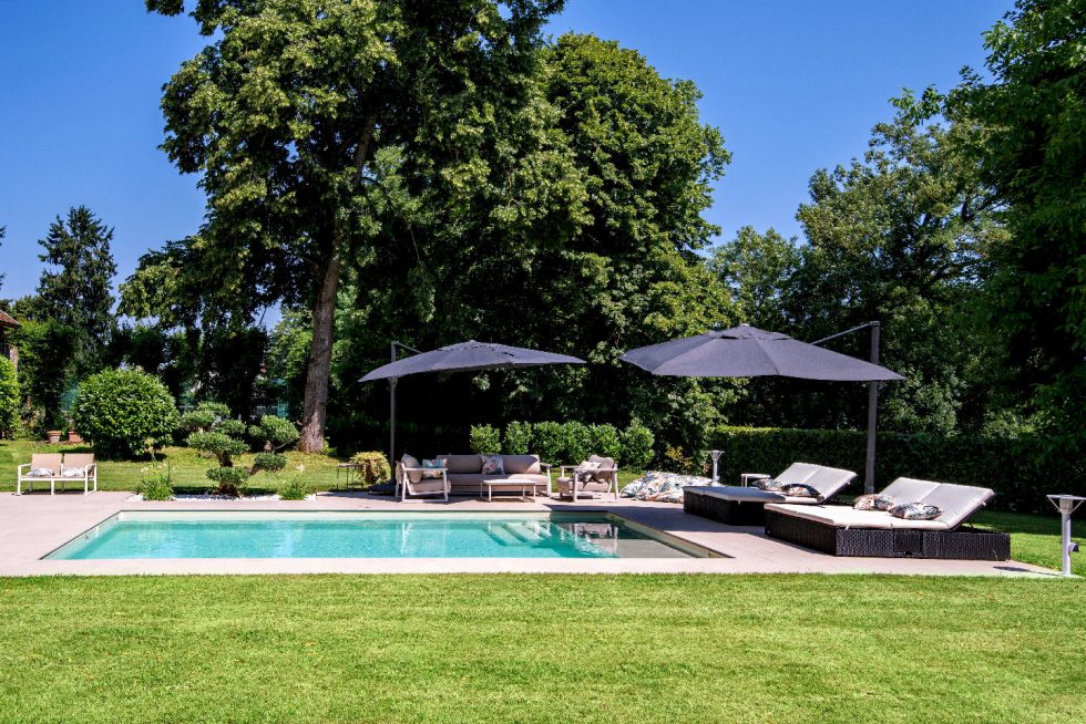 Terrasse aménagée avec salon de jardin, transats et parasols au bord d'une piscine béton Mondial Piscine à Buellas dans l'Ain, proche de Bourg-en-Bresse