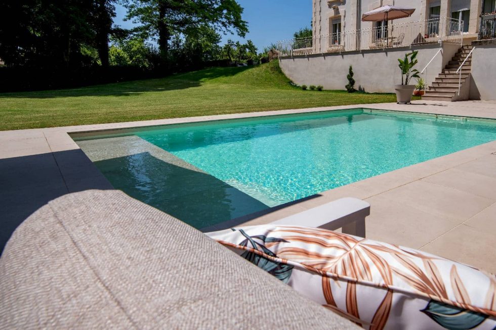 Vue depuis un transat sur la plage immergée de la piscine béton avec revêtement beige à Buellas