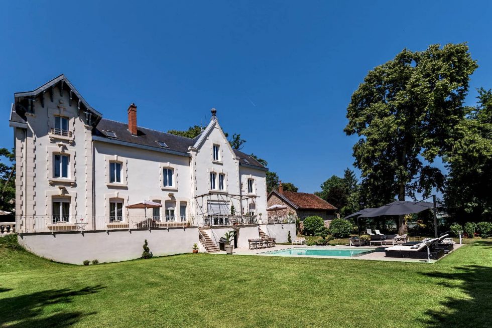 Vue d’ensemble d’une piscine béton Mondial Piscine devant une maison ancienne rénovée à Buellas