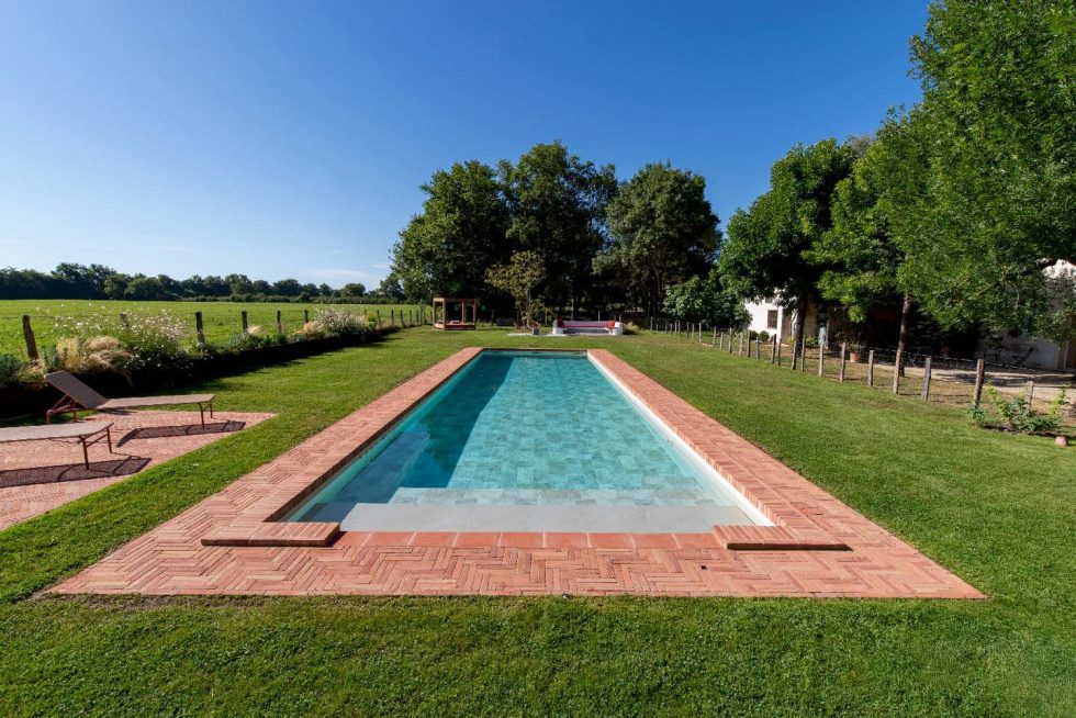 Piscine rectangulaire entourée de margelles en briques dans un cadre champêtre