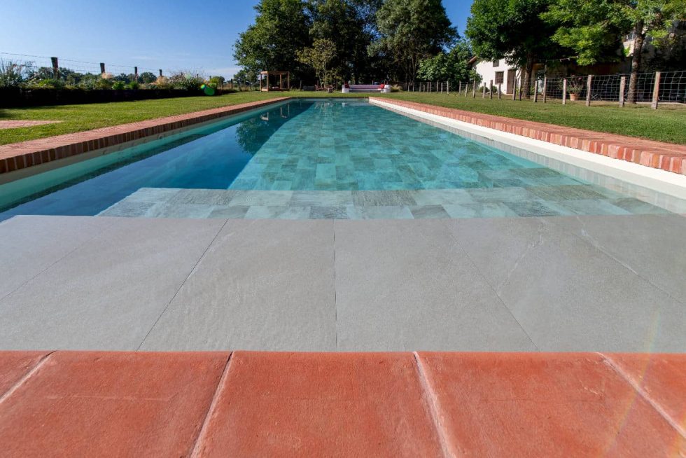 Vue sur la piscine rectangulaire entourée de briques et espace détente avec terrasse