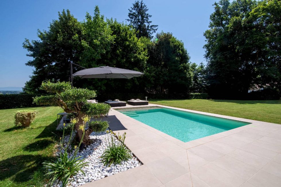 Piscine moderne avec grès cérame et massif végétal, intégrée à un jardin paysager à Buellas