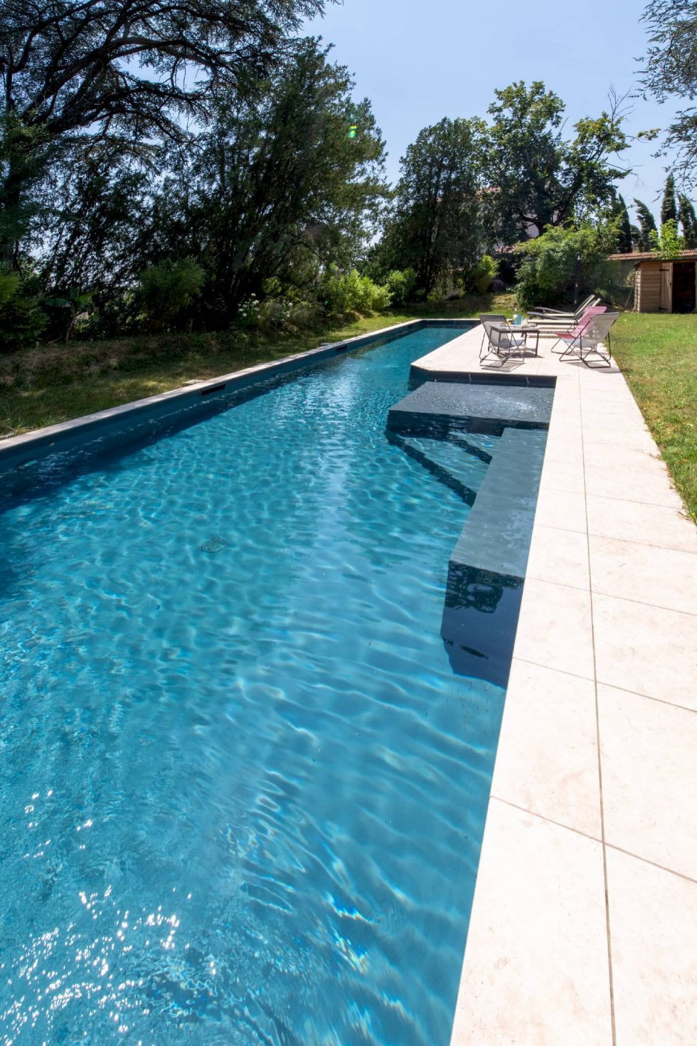 Perspective latérale sur la piscine couloir de nage et sa banquette immergée, entourée d’arbres à Beynost